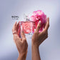 A woman's hand holding the La Vie Est Belle Rose Extraordinaire perfume bottle, showing its pink and white sculpted rose cap.