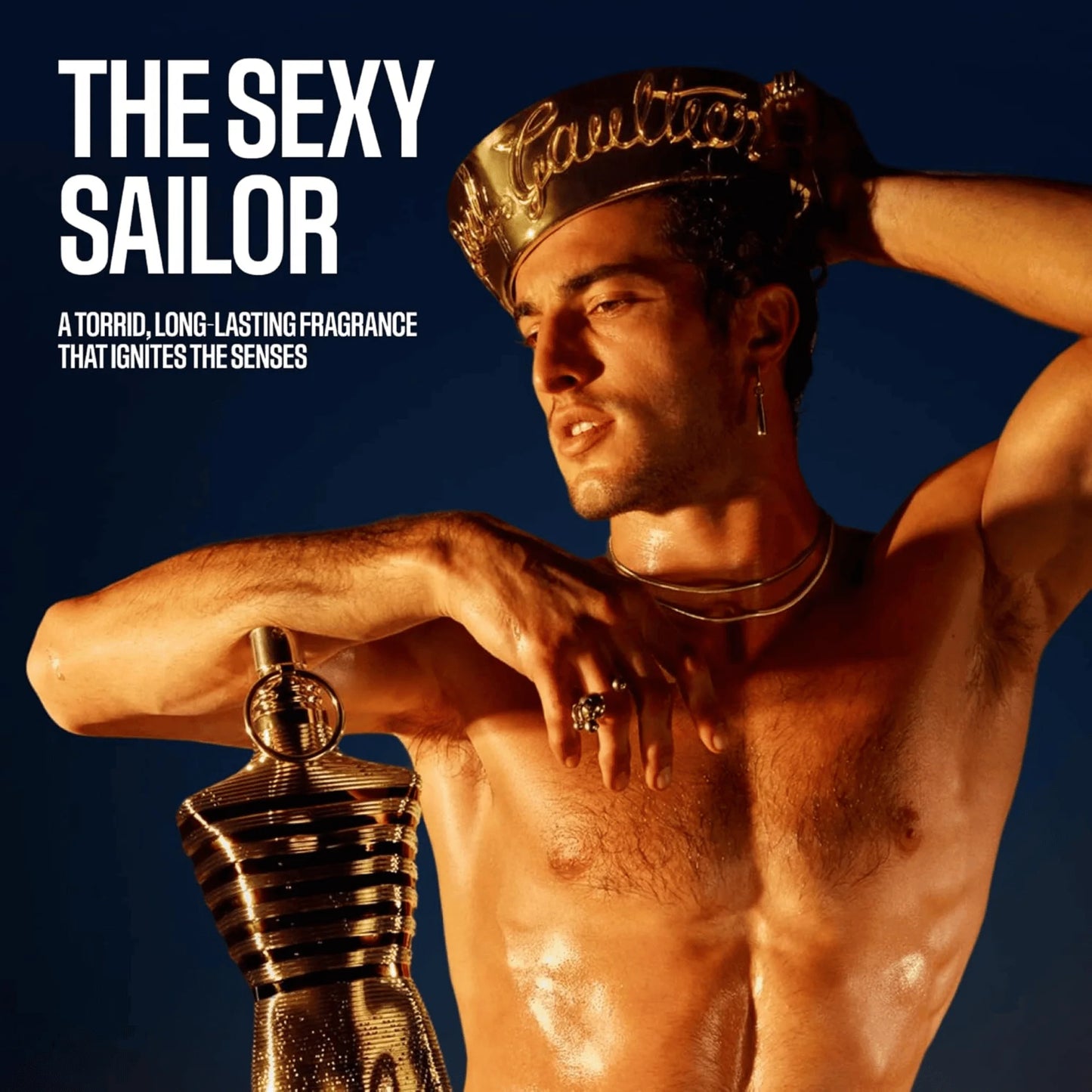 Promotional fragrance image for 'The Sexy Sailor' by Caudric, featuring a shirtless man wearing a gold Caulric crown and holding a gold mannequin-shaped perfume bottle against a dark blue background with bold white text.