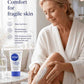 Woman applying moisturizer to her leg with a bottle of Dermender product on a marble surface.