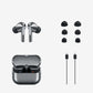 True wireless earbuds in metallic gray shown with an open charging case, six black ear tips, and two charging cables on a light gray background.