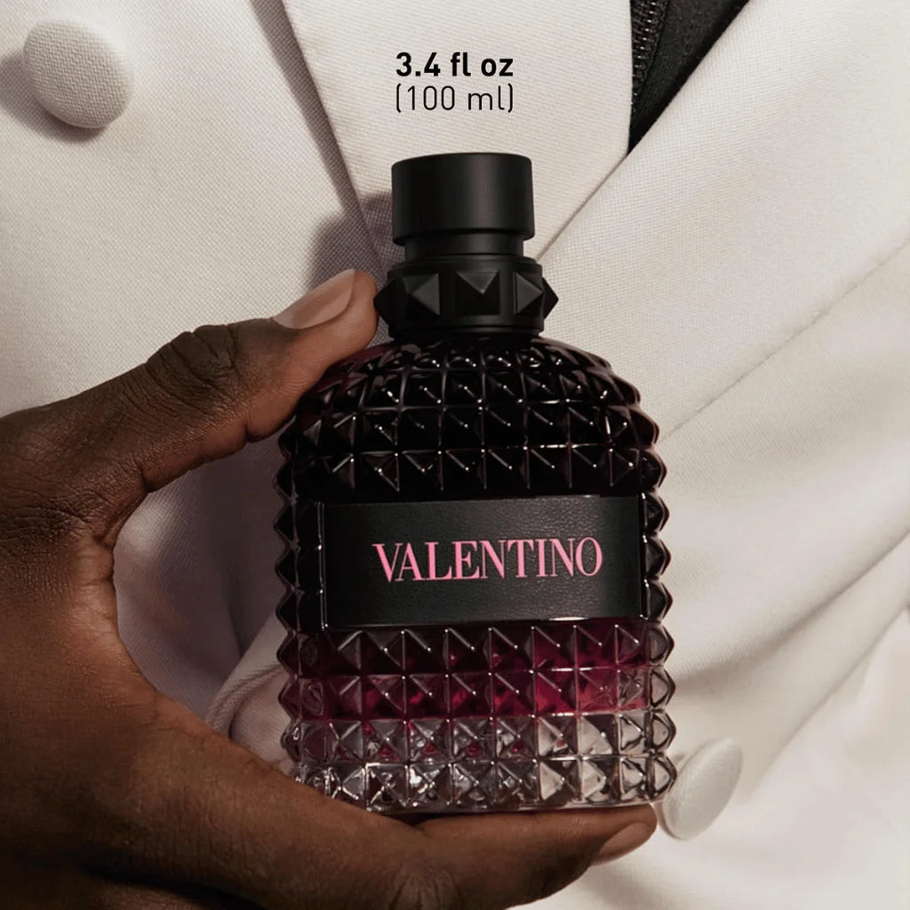 A hand holds a textured Valentino perfume bottle with a black cap and a black label featuring pink lettering, set against a white blazer. Text at the top reads '3.