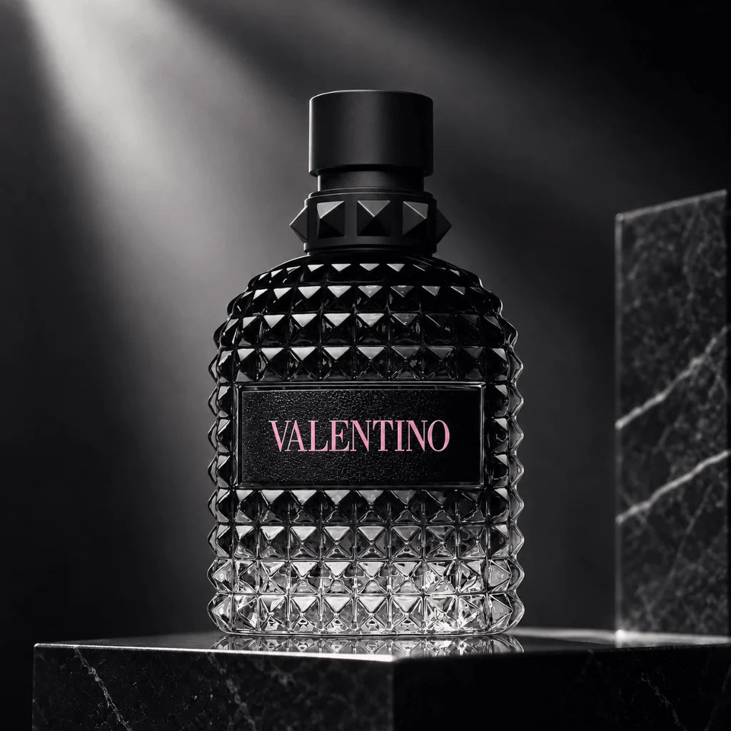 A textured black glass perfume bottle with a faceted diamond pattern, a black cap, and a black label featuring the brand name 'VALENTINO' in pink, displayed on a dark marble pedestal.