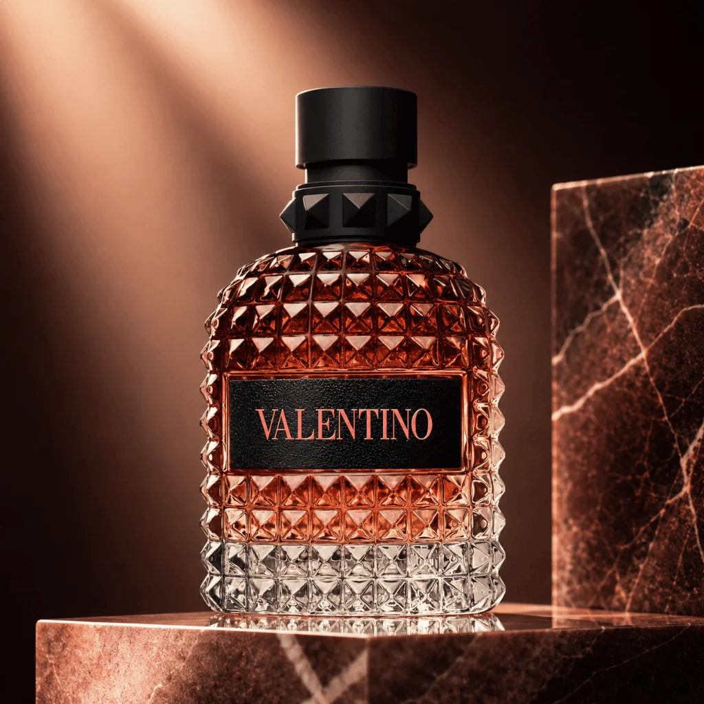 Valentino fragrance bottle with a faceted clear glass body, amber liquid, and a black cap, displayed on a metallic pedestal against a warm brown background with a marble block prop.