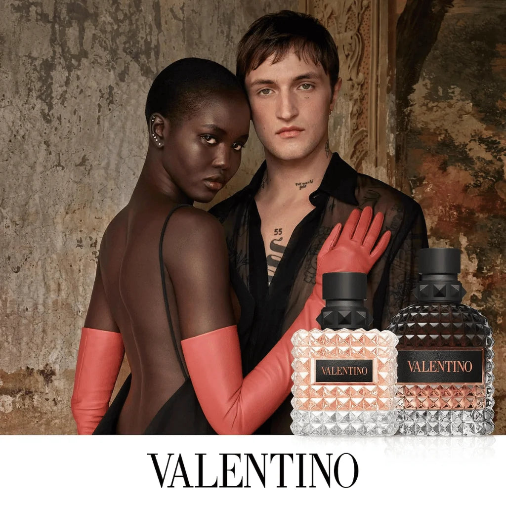 Two models pose with Valentino fragrance bottles in a textured interior setting. One model wears a black outfit with bright pink gloves, and the other wears a black sleeveless dress.