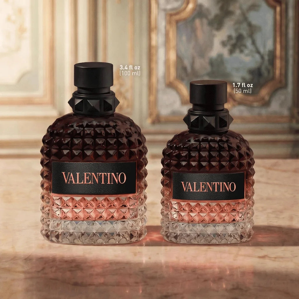 Two Valentino perfume bottles with textured rose-gold and clear glass bodies, black caps, and black labels with gold lettering, displayed on a marble surface with a classical interior background.