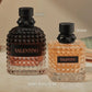 Two textured glass perfume bottles with black caps on a beige surface. The left bottle is dark brown with rose-gold-toned lower glass and a black label reading VALENTINO.